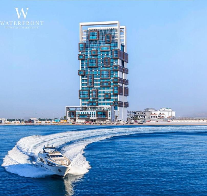 a boat in the water in front of a tall building at Waterfront Hotel Apartment in Lusail