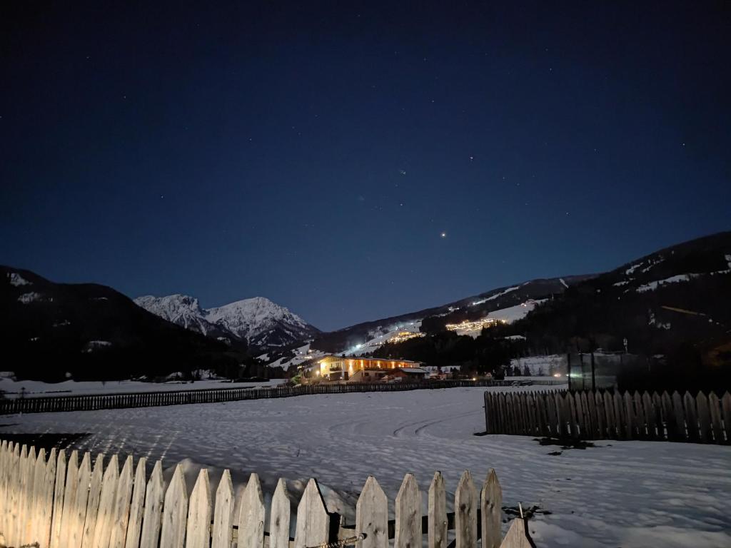 a snow covered street at night with a fence and mountains at Lerchnhof in Valdaora