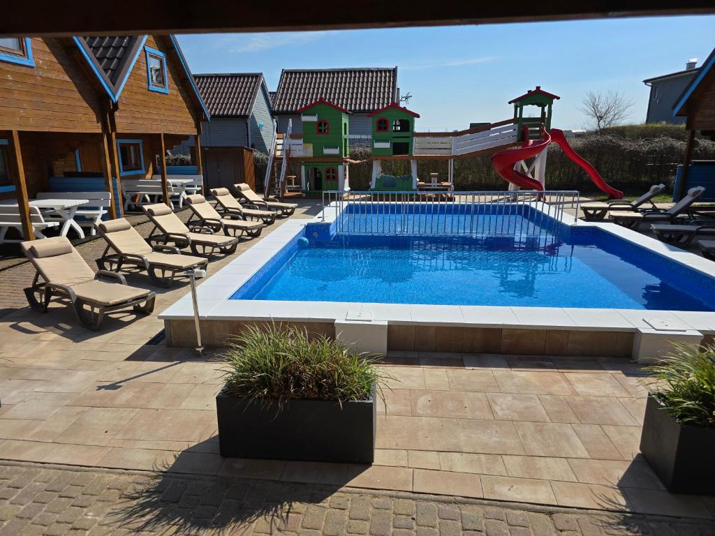 une piscine avec un toboggan, des chaises et une aire de jeux dans l'établissement Domki Rekin Podgrzewany basen z brodzikiem oraz klimatyzacją, à Rewal