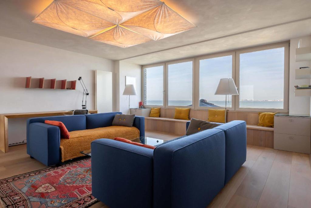 a living room with a blue couch and a living room with windows at Hello Zeeland - Appartement Port Scaldis 01-081 in Breskens