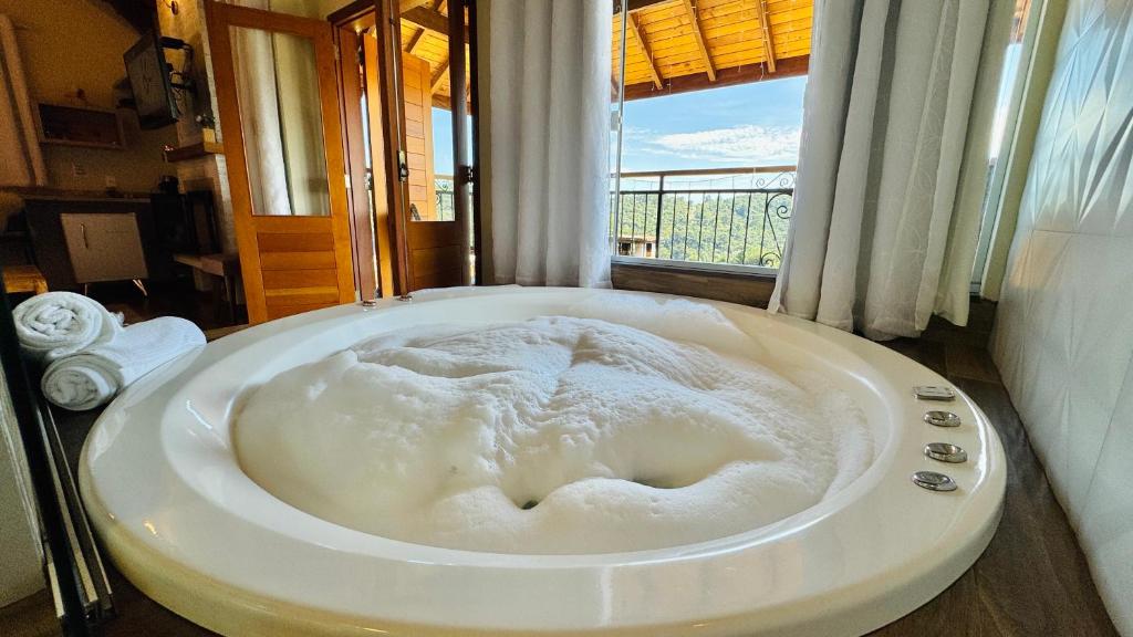 a large white bath tub in a room with a window at Chalés Vila do Moinho in Monte Verde