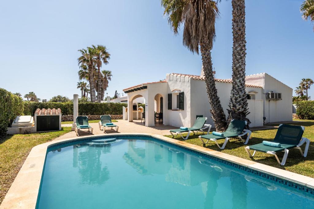 a swimming pool in front of a house with palm trees at Villa Miguel in Cala en Bosc