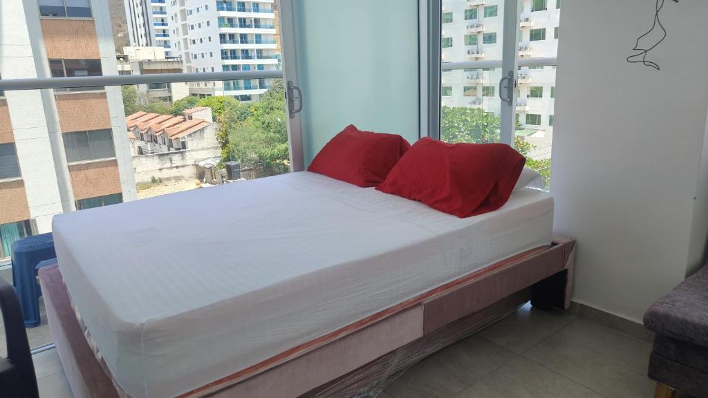 a bed with red pillows in a room with a window at Apartamento El Rodadero con balcón in Gaira