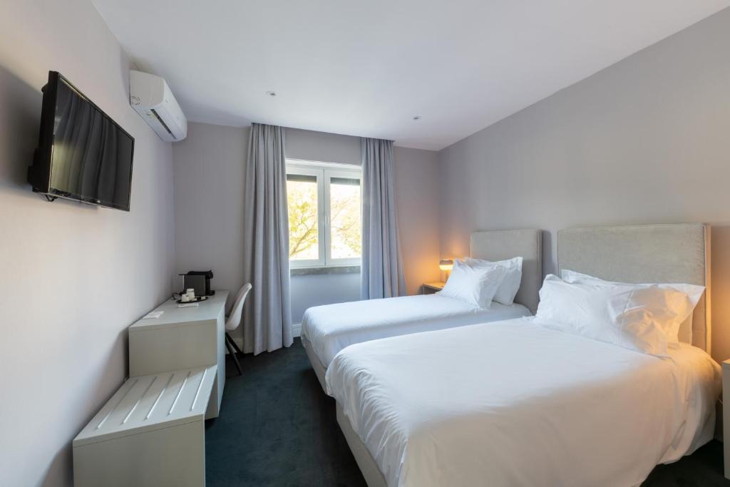 A compact twin bedroom with two beds, a desk, television and window.
