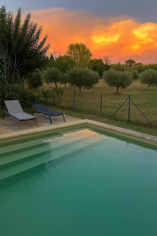 - une piscine avec 2 chaises et un coucher de soleil dans l'établissement Le Moulin de L'aire, à Lourmarin