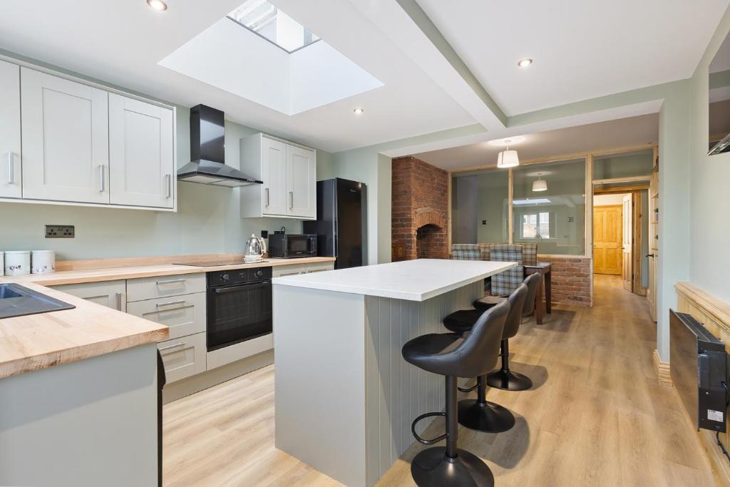 una cucina con armadi bianchi e una grande isola con sgabelli da bar di Pickin Cottage a Altofts