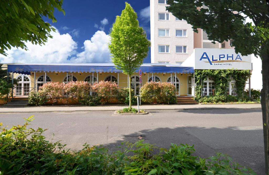 ein Gebäude mit einem Baum in der Mitte einer Straße in der Unterkunft Alpha Hotel garni in Dietzenbach