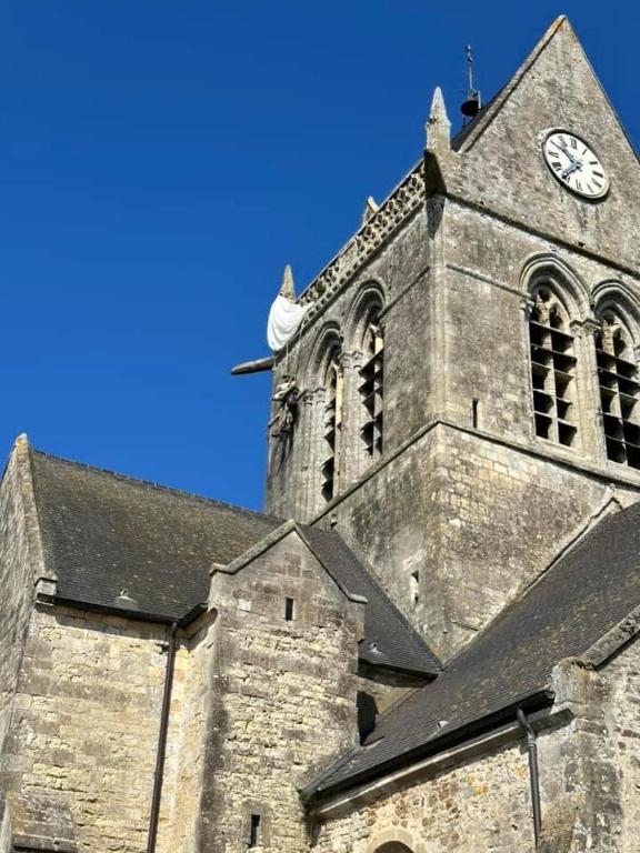 Une église avec une tour avec une horloge. dans l'établissement Maison de Famille face à l'église, à Sainte-Mère-Église
