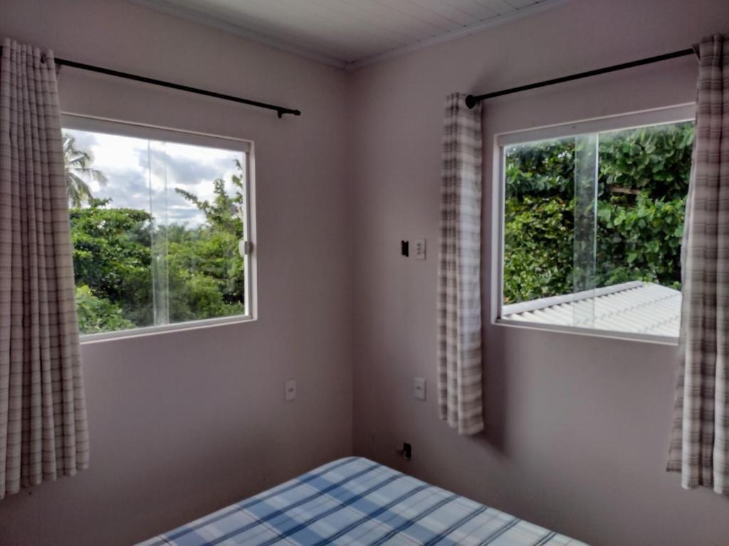 um quarto com uma cama e duas janelas em Casa do Sossego na Praia Guarajuba Barra do Jacuipe em Camaçari