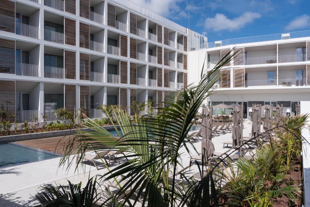an exterior view of a hotel with a palm tree at Mercure Ponta Delgada Azores in Ponta Delgada