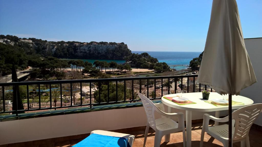 einen Balkon mit einem Tisch, Stühlen und Meerblick in der Unterkunft Apartamentos Encanto Del Mar in Cala Galdana