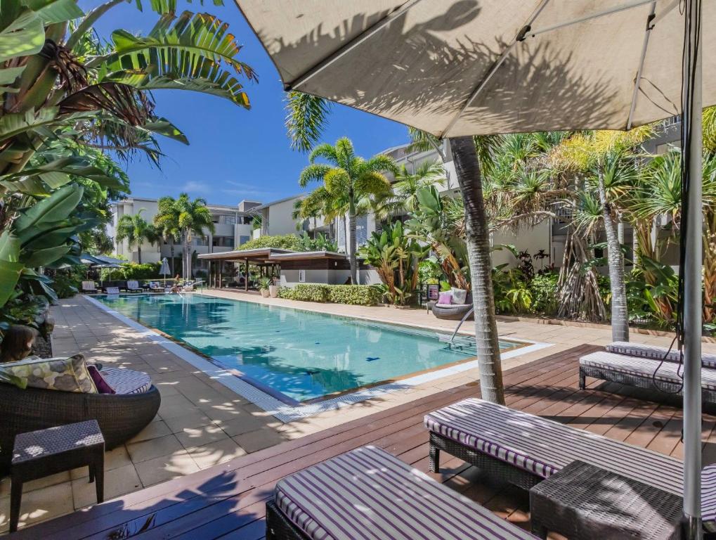 a pool at a resort with benches and an umbrella at Bali Luxury Resort - Holiday Management in Kingscliff