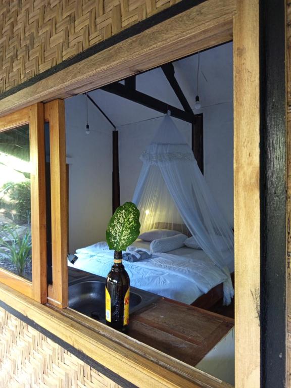 a room with a bed and a bottle with a plant in a window at are twin bungalows in Tetebatu