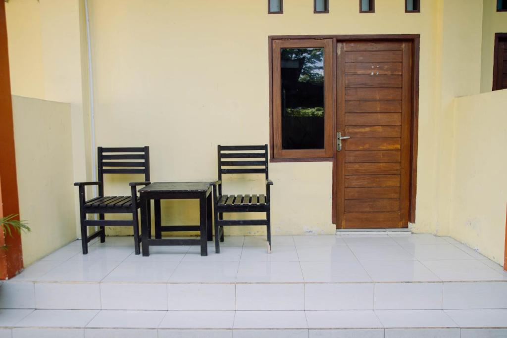 three chairs and a table and a wooden door at RedDoorz at Hening Homestay in Montongbuwoh