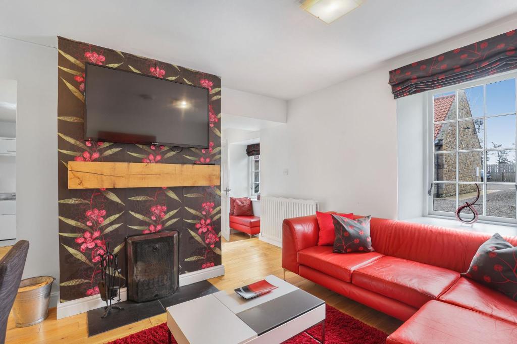 a living room with a red couch and a flat screen tv at Stewards Cottage - North East Escapes in Bamburgh