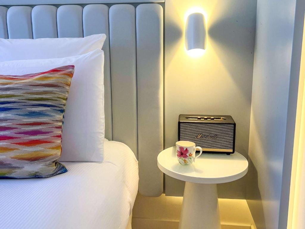 a bed with a table with a cup and a clock at Croisette Beach Hotel Cannes - MGallery Collection in Cannes