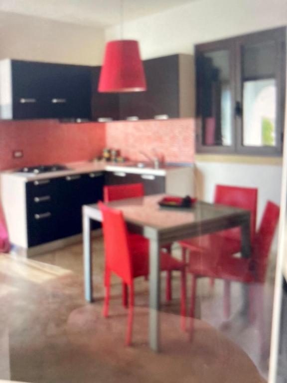 a kitchen with a dining table and red chairs at L'Asfodelo in Uggiano la Chiesa