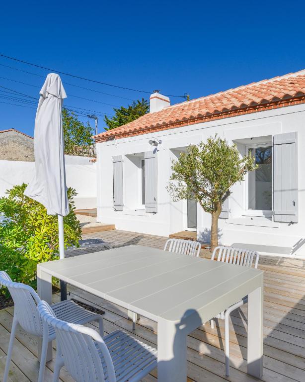 une table blanche avec des chaises et un parasol sur une terrasse dans l'établissement Barbâtre - Les Figuiers, à Barbâtre