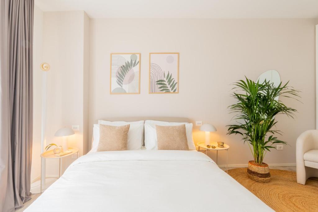 a white bedroom with a large bed and a plant at Vibra Tahiti Prestige in Lido di Jesolo