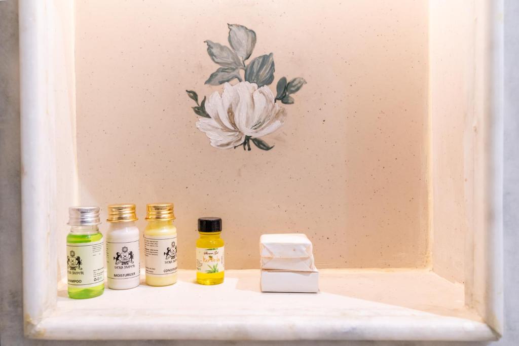 three bottles of essential oils on a shelf with a flower on the wall at Dera Jaipur Homestay in Jaipur