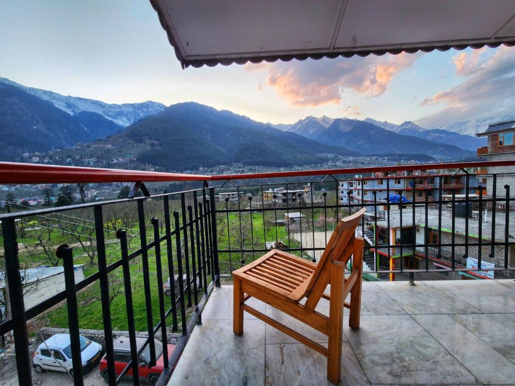 a wooden bench sitting on a balcony with a view of mountains at Kundan Hotel and Restaurant in Manāli
