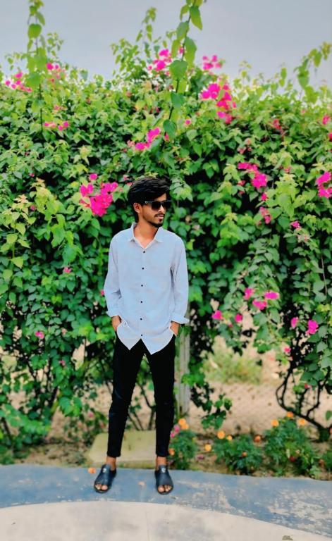 un hombre parado frente a un arbusto con flores rosas en Jurain Dhaka, en Dhaka