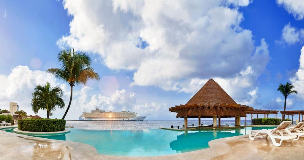 a resort swimming pool with a cruise ship in the background at Grand Park Royal Cozumel - All Inclusive in Cozumel