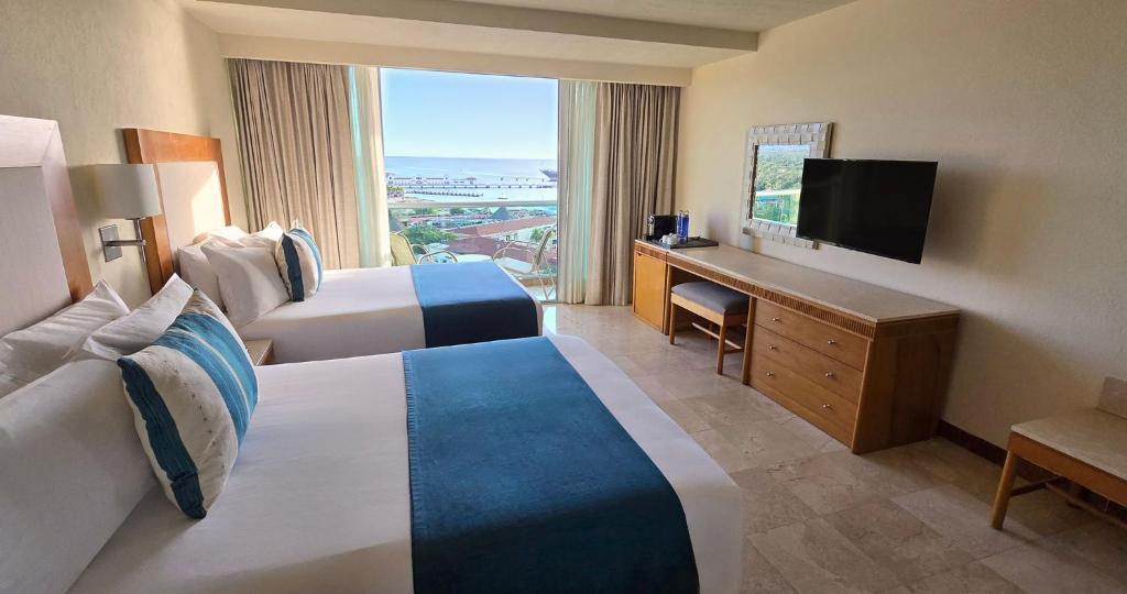 a hotel room with two beds and a flat screen tv at Grand Park Royal Cozumel - All Inclusive in Cozumel