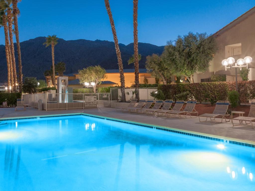 a swimming pool with palm trees and a building at Downtown Winner at Plaza Villas by ACME House Company in Palm Springs