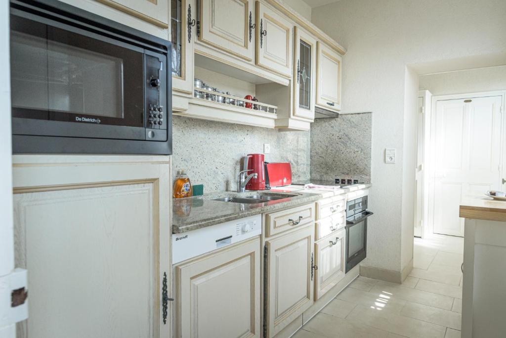a kitchen with white cabinets and a microwave at Maison Studios & Appartements Les 4 Vents in Luc-sur-Mer