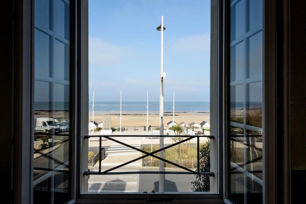 an open window with a view of the beach at Maison Studios & Appartements Les 4 Vents in Luc-sur-Mer