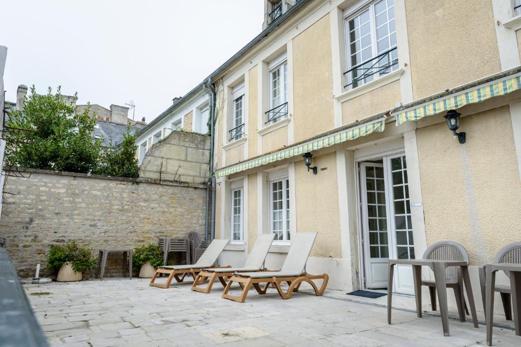 a group of chairs and tables on a patio in front of a building at Maison Studios & Appartements Les 4 Vents in Luc-sur-Mer