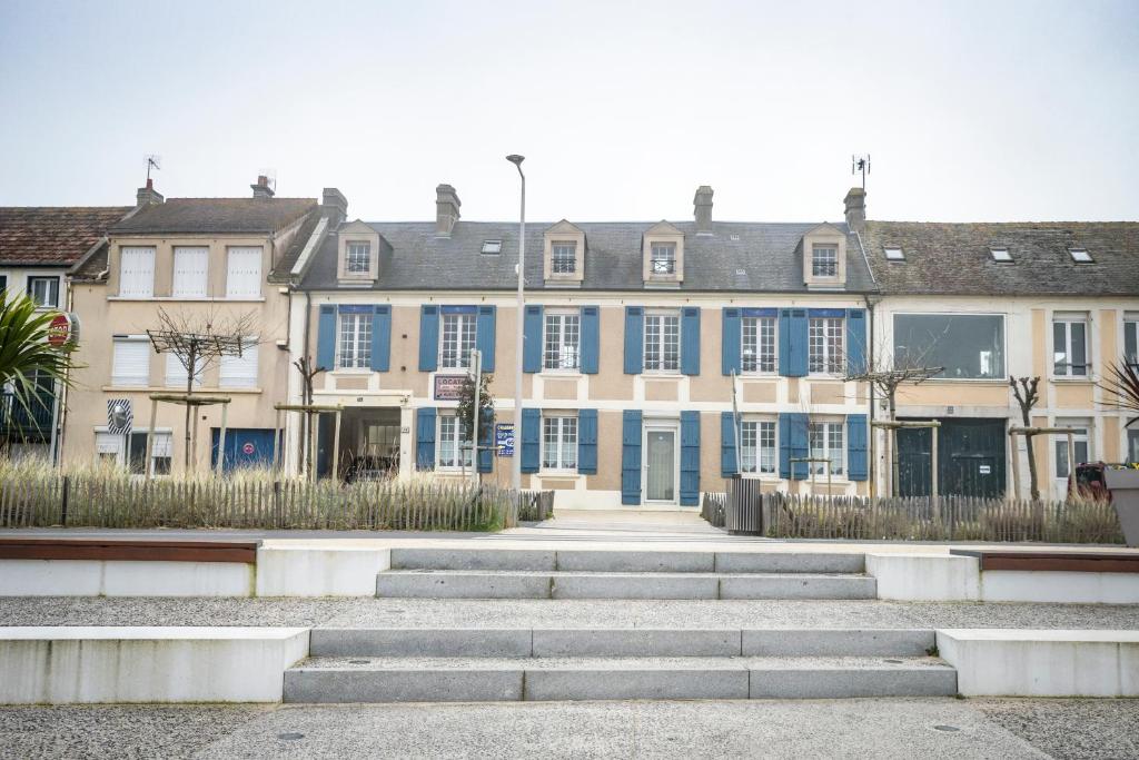a large building with blue windows and stairs in front at Maison Studios & Appartements Les 4 Vents in Luc-sur-Mer