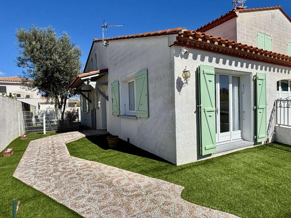 une maison blanche avec des portes vertes et une cour dans l'établissement Élégant T2 avec Jardin, Secteur Calme, Proche Mer et Commerces - Latour-Bas-Elne - FR-1-225-650, à Latour-Bas-Elne