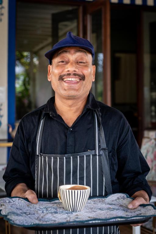 a man in an apron holding a cup of coffee at Dera Jaipur Homestay in Jaipur