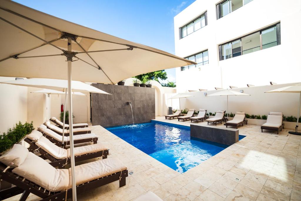 uma piscina com cadeiras e guarda-sóis ao lado de um edifício em Aspira Hotel Playa del Carmen em Playa del Carmen