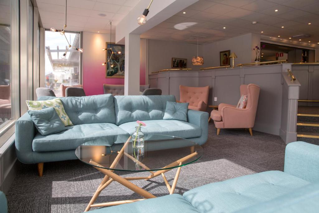 a living room with a blue couch and pink chairs at First Hotel Dragonen in Umeå