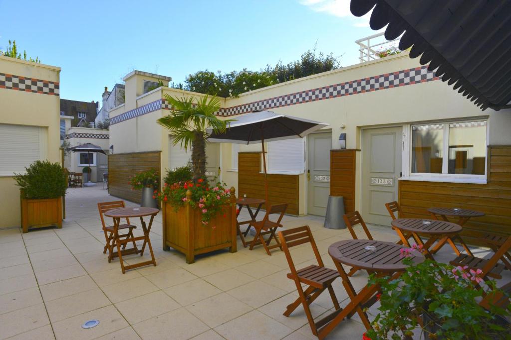 a patio with tables and chairs and an umbrella at Almoria Hôtel & SPA in Deauville