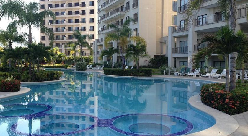 a large swimming pool with palm trees and buildings at Luxury Condo Jaco Beach in Jacó