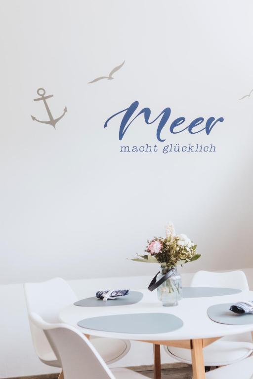a white table with white chairs and a vase of flowers at Küsten Auszeit in Wremen