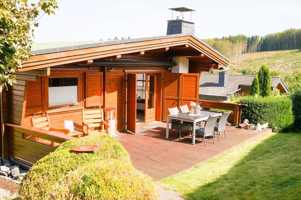 a house with a wooden deck with a table and chairs at Holzhaus Hubertus mit Sauna und Kamin in Meschede