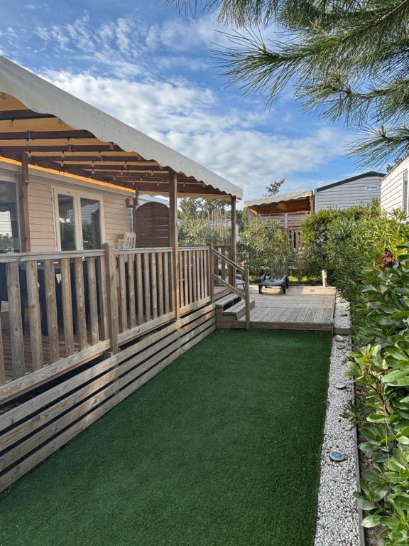 a backyard with a deck and green lawn at Lodge du Sangla Mobil Home premium Village Vacances 4 étoiles Lège Cap Ferret in Lège-Cap-Ferret