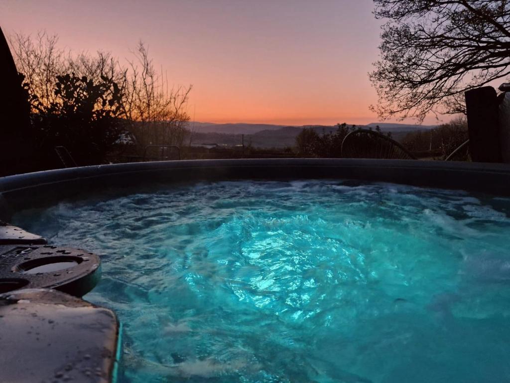 a hot tub with blue water with a sunset in the background at Odli Glamping - Deri in Welshpool