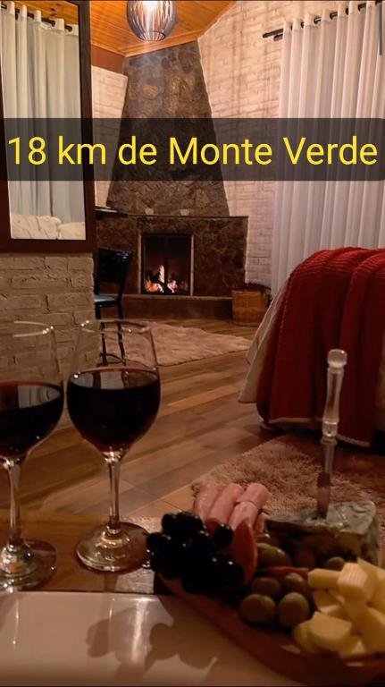 two glasses of wine on a table with a fireplace at Chalé Sonho Diniz 3 in Monte Verde