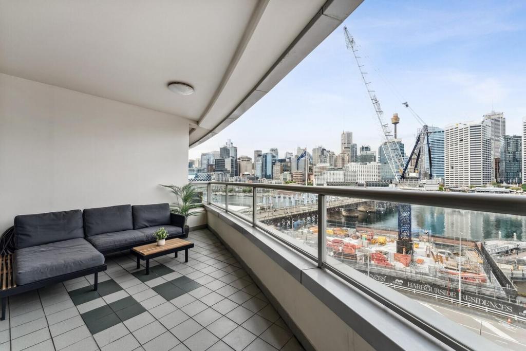 a balcony with a couch and a view of a city at Darling Harbour Views 2BR 2Bath, Pool, Parking, Spa & Gym in Sydney