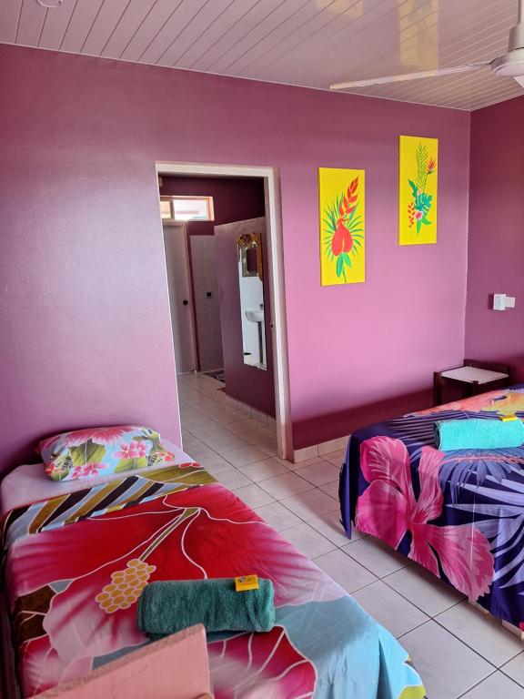 a room with two beds and a pink wall at Pension Tautiare Village in Maupiti
