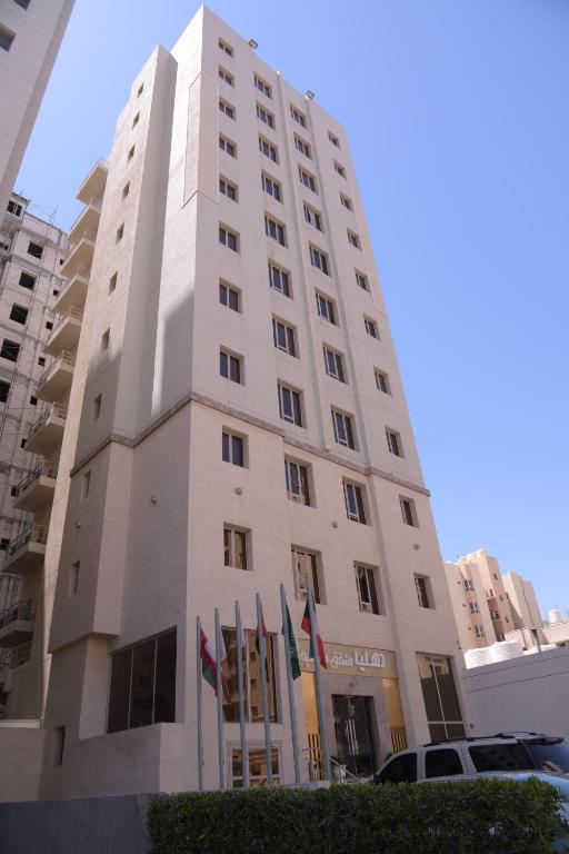 a tall white building with flags in front of it at Dahlia Hotel Apartment Riggae in Kuwait