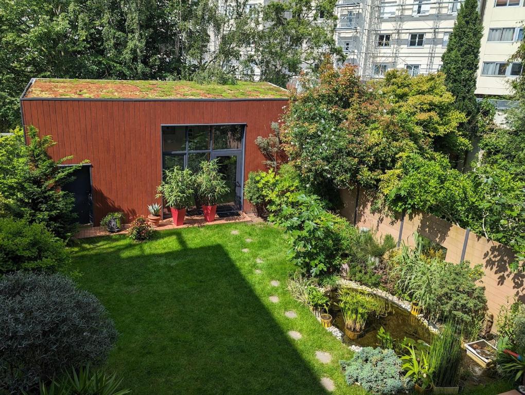 un jardin avec un petit bâtiment rouge orné de plantes dans l'établissement Tiny House dans le jardin, à Boulogne-Billancourt