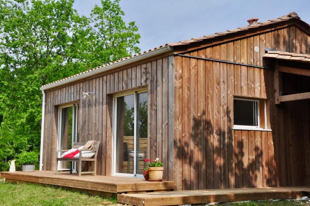 a wooden tiny house with a porch and a chair at Le Séchoir, au Jardin des Tisanes in Tabanac