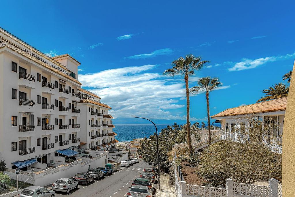 una calle con coches estacionados junto a edificios y el océano en La Perla Beach Vibes, en Puerto de Santiago